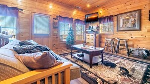 A cozy log cabin interior with a bed, a coffee table, a TV, and a Christmas tree. - Smokey's Hideaway (Sevierville)