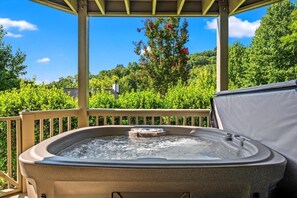Ein Whirlpool unter einer Holzhütte mit Blick auf einen üppigen Garten und eine sanfte Hügelkulisse.