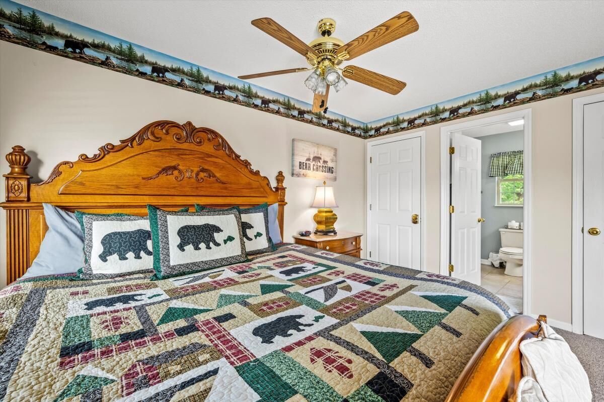Een slaapkamer met een houten hoofdeinde, een quilt met berenmotieven, een plafondventilator en een deur naar een andere kamer.