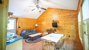 L'intérieur d'une cabane en bois, avec une table à manger, un canapé et un ventilateur de plafond.