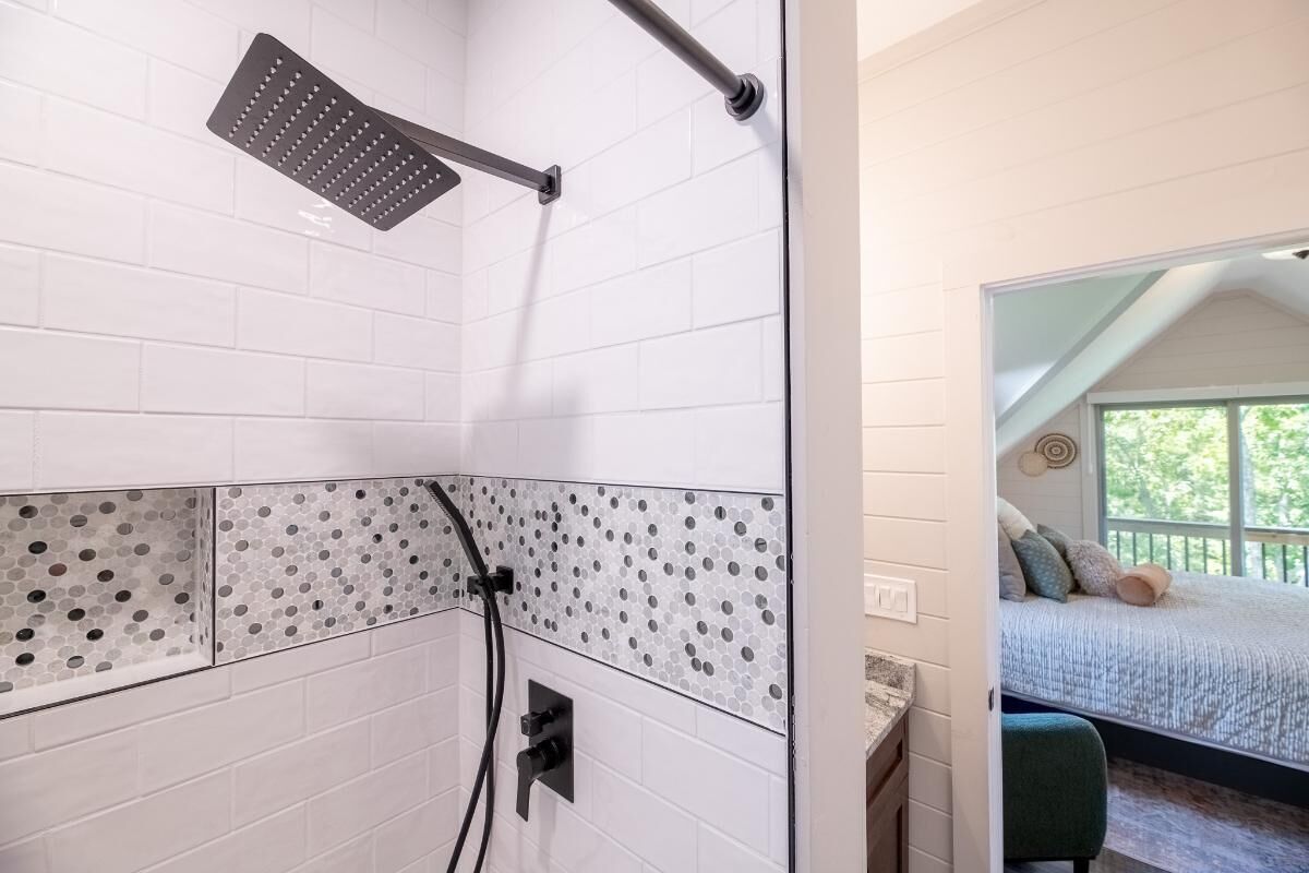 Een badkamer met witte betegelde wanden, een douchekop en een decoratieve tegelrand.