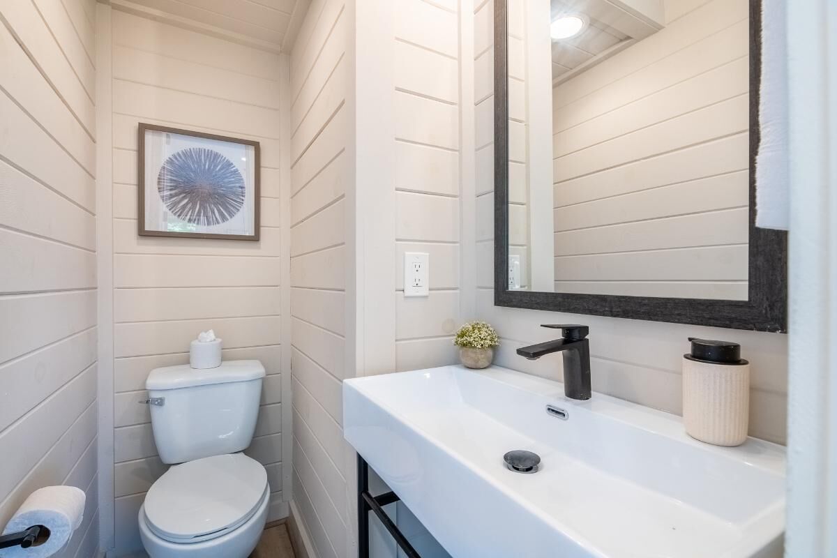 A bathroom with a white toilet, a sink with a mirror, and a framed picture on the wall.
