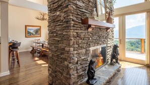 A stone fireplace with a bear sculpture, a dining area with wooden furniture, and a large window with a mountain view. - Window Wonderland (Gatlinburg)