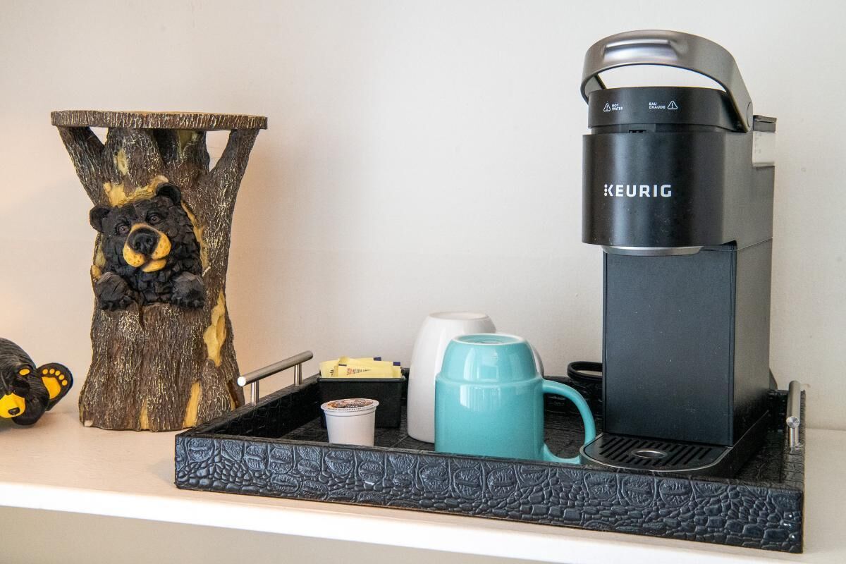 Eine Kaffeemaschine, eine Tasse, eine Becher und eine Bär-Figur auf einem Regal.