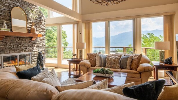 A spacious living room with a stone fireplace, large windows, and a chandelier. - Window Wonderland (Gatlinburg)