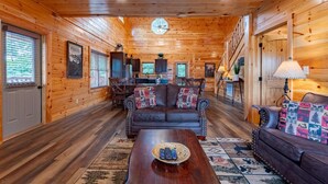 A log cabin interior with a wooden ceiling, a leather sofa, a coffee table, and a dining area. - Smokey Waters (Sevierville)