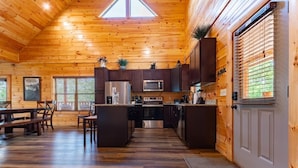 A wooden cabin interior with a kitchen, dining area, and a large window. - Smokey Waters (Sevierville)