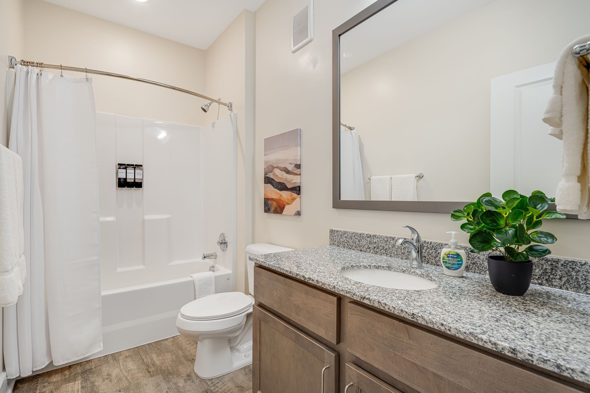 A bathroom with a shower, toilet, sink, and a potted plant.