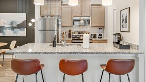 Een moderne keuken met granieten aanrechtbladen, roestvrijstalen apparatuur en hangende lampen.