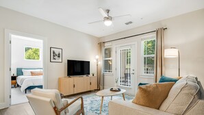 Een moderne woonkamer met een flatscreen televisie, een bank, een fauteuil, een klein tafeltje en een plafondventilator.
