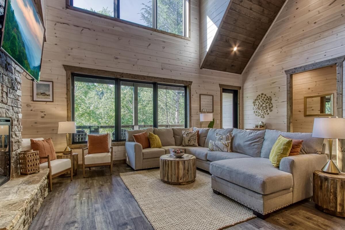 A spacious living room with a large sectional sofa, a fireplace, and large windows offering a view of the outdoors.