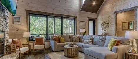 Un salon spacieux, doté d’un grand canapé d’angle, d’une cheminée et de grandes fenêtres offrant une vue sur l’extérieur.