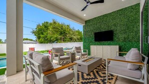 Eine Terrassengrundstück mit Pool, Sitzgelegenheit und einer grünen Wand mit einem Flachbildfernseher.