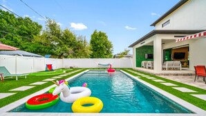 Ein Schwimmbecken mit Rasenkanten, eine Lounge mit Gartenmöbeln und ein weißer Zaun.