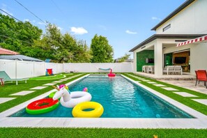 Ein Schwimmbecken mit Rasenkanten, eine Lounge mit Gartenmöbeln und ein weißer Zaun.