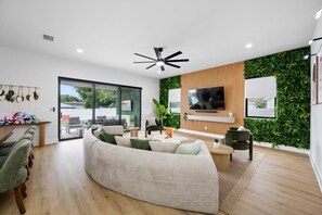 A modern living room with a curved sofa, a flat-screen TV, and a ceiling fan. - Luxe Villa • Pool&Spa • Sauna • Games • Sleeps 20+ (Tampa)