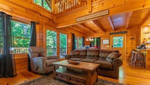 A log cabin interior with a sofa set, a chair, a coffee table, and a kitchen area with a sign reading 'Bless the family gathered here.' - Sweet Bear Hideaway (Sevierville)