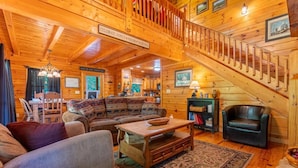 A log cabin interior with a wooden staircase, a sofa set, a dining table, and a fireplace. - Sweet Bear Hideaway (Sevierville)