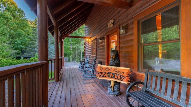 A wooden cabin with a porch, a bench, and a sign that reads 'Sweet Bear Hide-A-Way.' - Sweet Bear Hideaway (Sevierville)