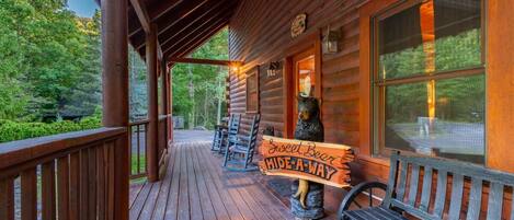 Een houten vakantiehuisje met een veranda, een bankje en een bordje met de tekst 'Sweet Bear Hide-A-Way'.