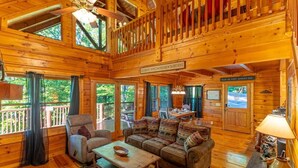 A spacious wooden cabin with a high ceiling, a cozy living area with a sofa and armchairs, a dining table, and a view of the outdoors. - Sweet Bear Hideaway (Sevierville)