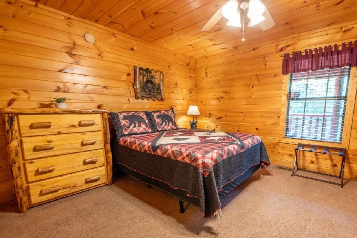 Un dormitorio de cabaña de madera con cama, cómoda, lámpara y ventana.
