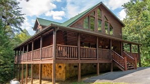Eine Blockhütte mit Balkon, Stein Fundament und einem grünen Dach.