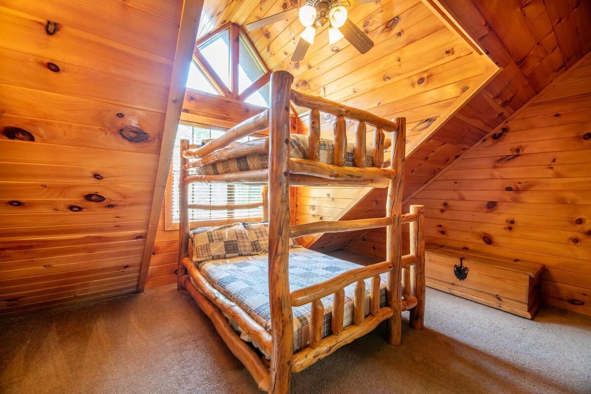 Interior de una cabaña de madera con literas, un ventilador de techo y una ventana.