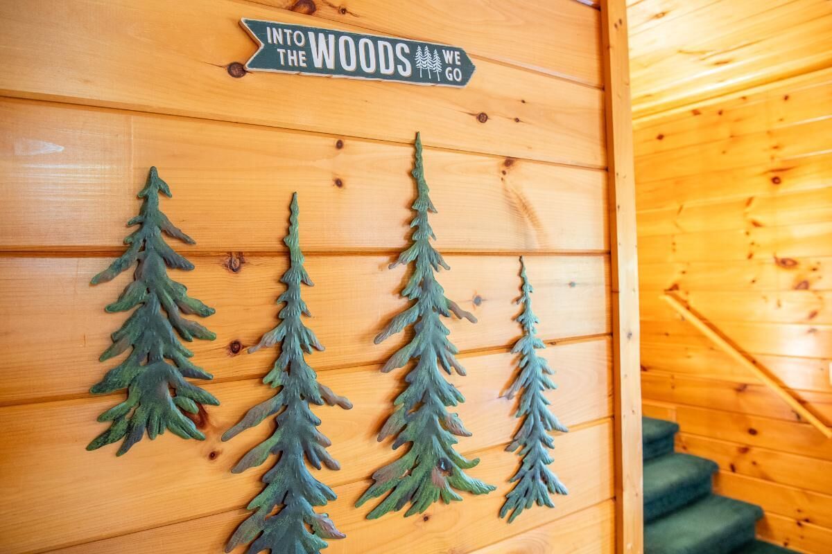 Een houten wand met een bord waarop staat 'Into the Woods We Go' en drie kunstpijnbomen.