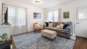 Una sala de estar con sofá, sillón, reposapiés y televisor sobre un mueble.