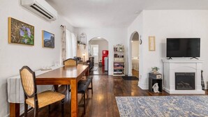 Un amplio salón con chimenea, un comedor con mesa y sillas de madera, y un televisor montado sobre la chimenea.