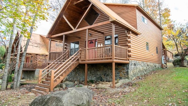 Eine Blockhütte mit Steinunterbau, einer Holzterrasse und einer Treppe zum Eingang.