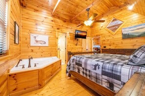 A wooden cabin interior with a bed, a bathtub, a ceiling fan, a TV, and a painting on the wall. - Rhythm & Blues (Gatlinburg)