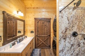 Ein Badezimmer einer Holzhütte mit einem großen Spiegel, einem Waschbecken, einer Holztür und einem Duschbereich.