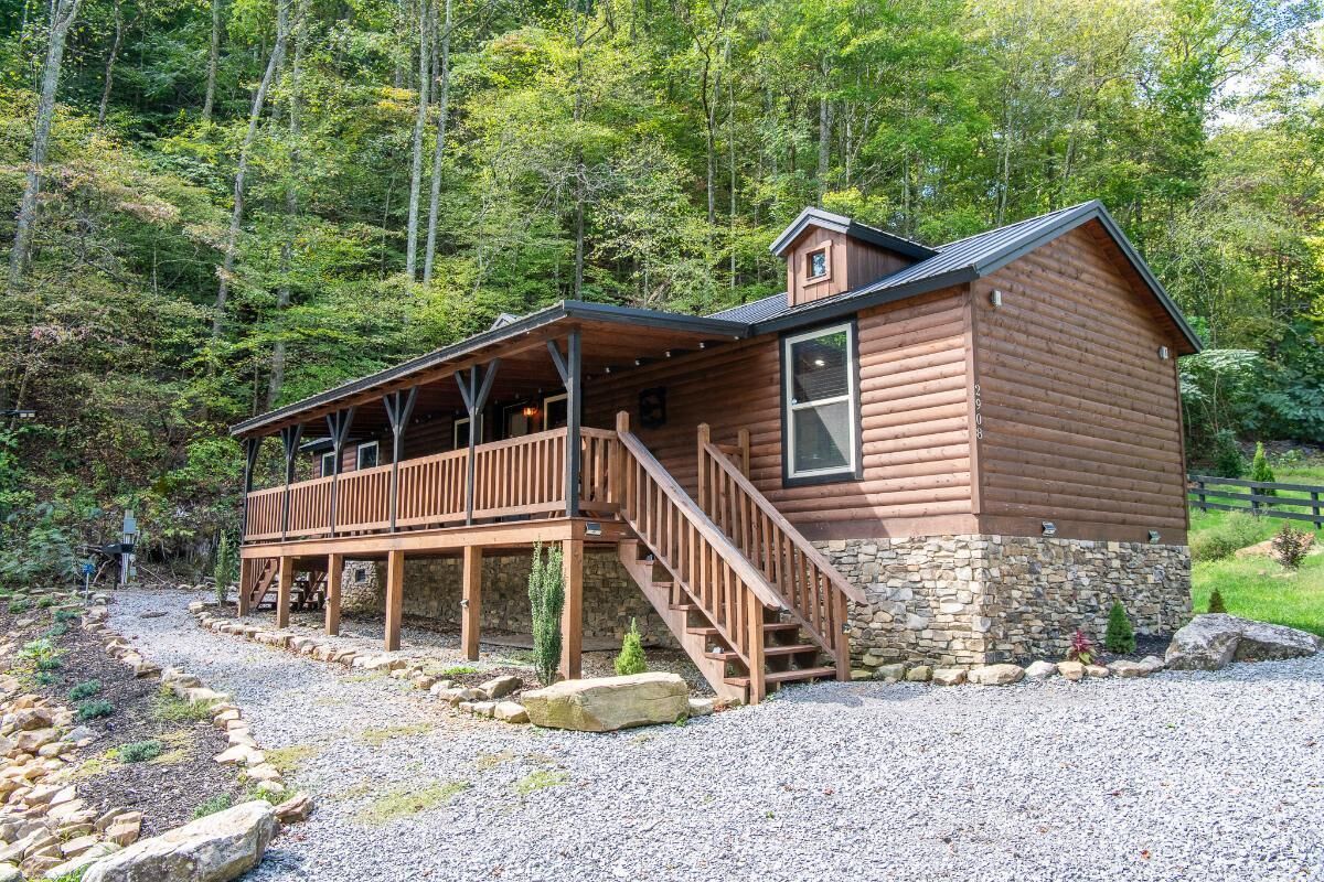 A wooden cabin with a porch, stone foundation, and a staircase leading to the entrance.