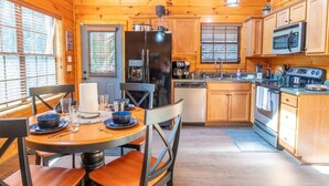 Een houten cabin interieur met een gedekte eettafel, keukenapparatuur en uitzicht op de natuur.
