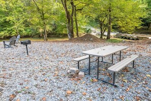 Ein Sitzbereich im Freien mit Tisch und Bänken, umgeben von Bäumen und Kies.
