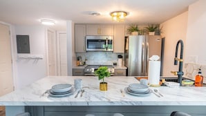 A modern kitchen with a marble countertop, stainless steel appliances, and a central island with seating. - The Jeffrey Martin (Gatlinburg)