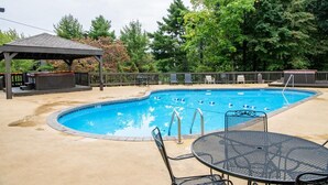 A swimming pool with a gazebo, outdoor seating, and trees in the background. - The Jeffrey Martin (Gatlinburg)