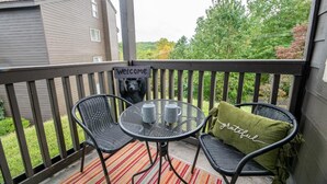 A balcony with a 'Welcome' sign, two chairs, a small table with two mugs, and a green pillow with 'grateful' written on it. - The Jeffrey Martin (Gatlinburg)