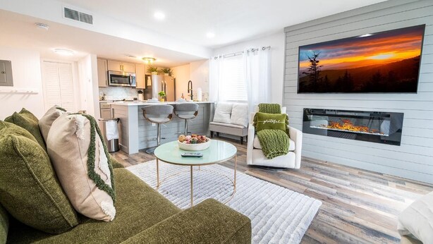 A modern living room with a sofa, a coffee table, a fireplace, and a kitchen in the background. - The Jeffrey Martin (Gatlinburg)