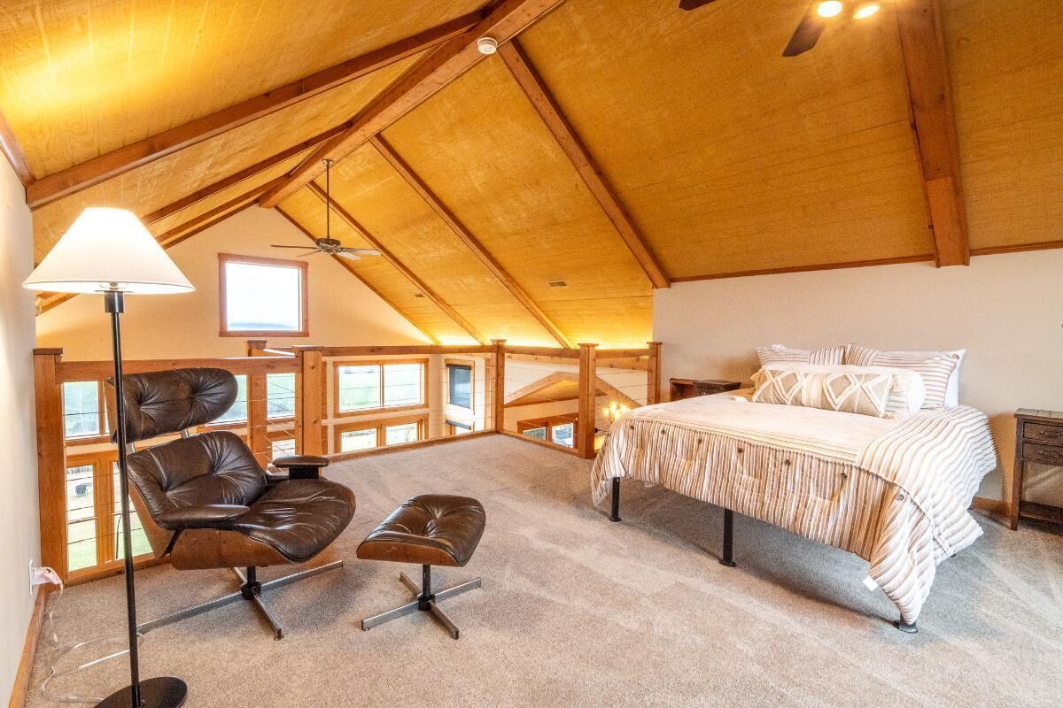 A bedroom with a bed, a chair, an ottoman, a lamp, and a ceiling fan.