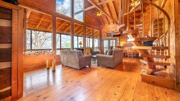 A wooden cabin interior with a wooden staircase, two sofas, and large windows. - Mountain Memories 2 (Sevierville)