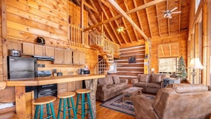 A log cabin interior with a kitchen, bar stools, a sofa, and a staircase. - Mountain Memories 2 (Sevierville)