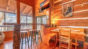 A wooden cabin interior with a dining area, bar stools, and a large window. - Mountain Memories 2 (Sevierville)