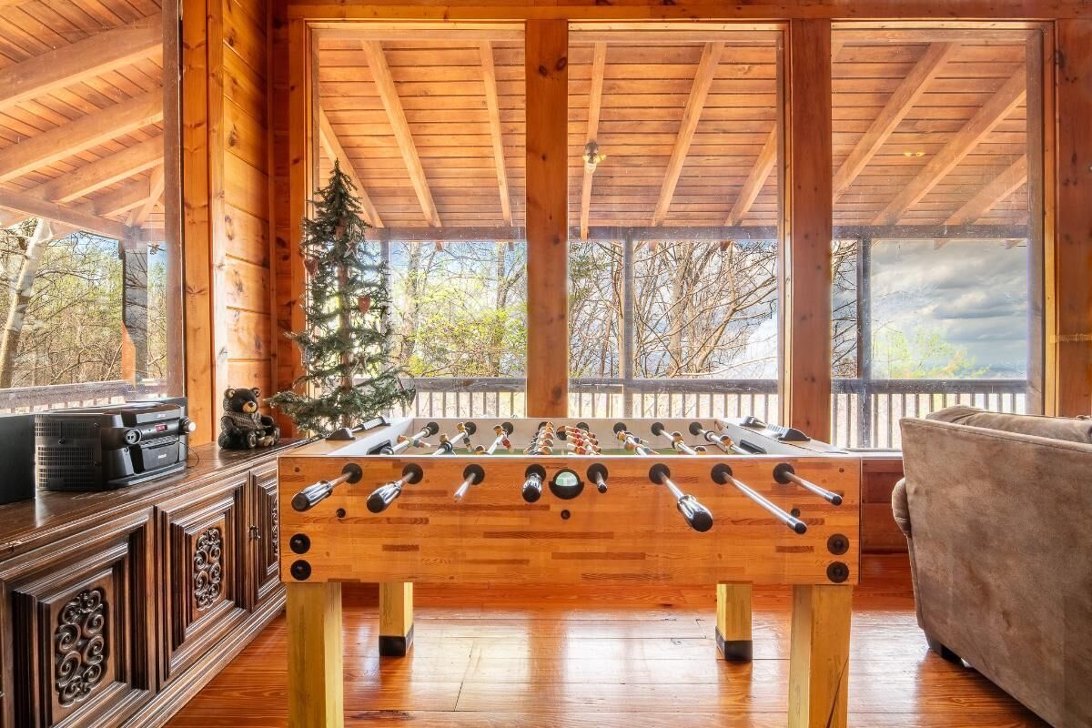 Une table de baby-foot en bois, dans une pièce dotée de grandes fenêtres et offrant une vue sur les arbres.