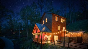 Eine zweistöckige Holzhütte mit Balkon, Lichterkette und Blick auf den umliegenden Wald.
