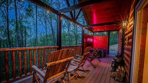 Eine Holzterrasse mit Stühlen, einem Kamin und Blick ins Waldgebiet.