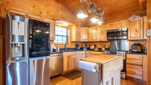 A modern kitchen with stainless steel appliances, wooden cabinets, and a roll of paper towels on a wooden cart. - Ridge Vista (Gatlinburg)