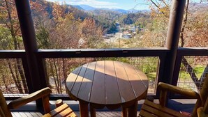 A wooden deck with a round table and two chairs, overlooking a valley with autumn foliage and distant mountains. - Ridge Vista (Gatlinburg)